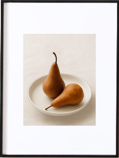 Cette affiche imprimée illustre deux poires complices déposées dans une assiette minimaliste. Les teintes chaleureuses et la lumière douce créant une atmosphère accueillante, invitant chacun à s’asseoir et à savourer un instant simple et gourmand.