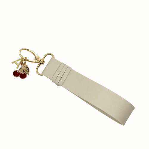 Porte-clés en simili cuir Vegan de couleur sable avec fermoir à pince, breloque logo Absolument doré et breloque cerises rouge et doré.