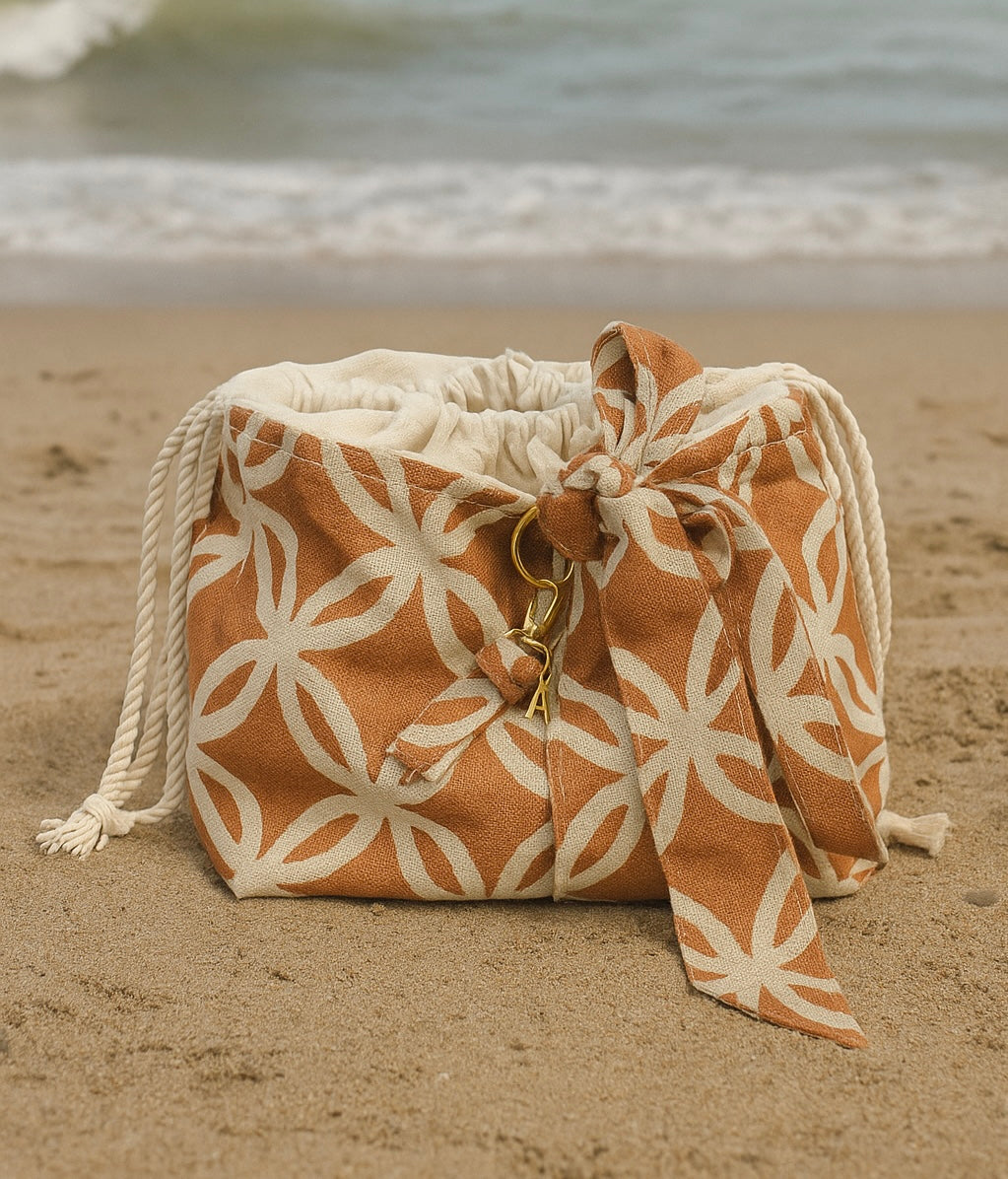 Ensemble Sac de plage SOLÉA fait à la main de façon artisanale au Québec. Le sac est Composé d'un tissu extérieur  en Lin terra cota et crème avec un motif arabesque. L'intérieur du sac est fait d'un coton crème et se referme avec un cordon de serrage de couleur crème. Un foulard pour nouer aux cheveux est suspendu au sac à l'aide d'une anneau dorée pouvant servir d'accessoire bijou au poignet. Inclus un POrte-clés fait du même tissu que le sac fini avec un fermoir à pince doré.