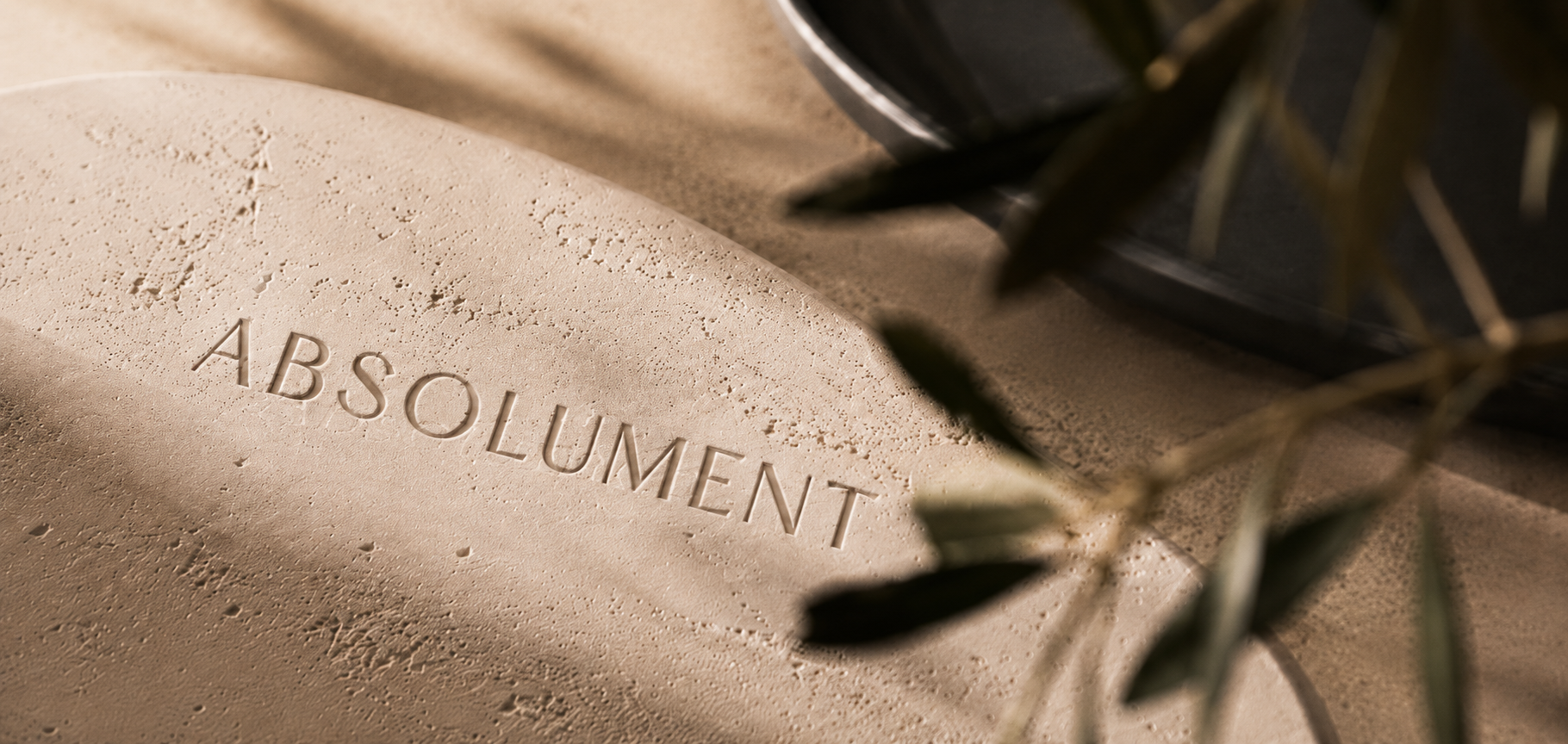Texture minérale crème avec logo Absolument embossé, inspirée des galets à parfumer et de la décoration apaisante de style hôtel-boutique.