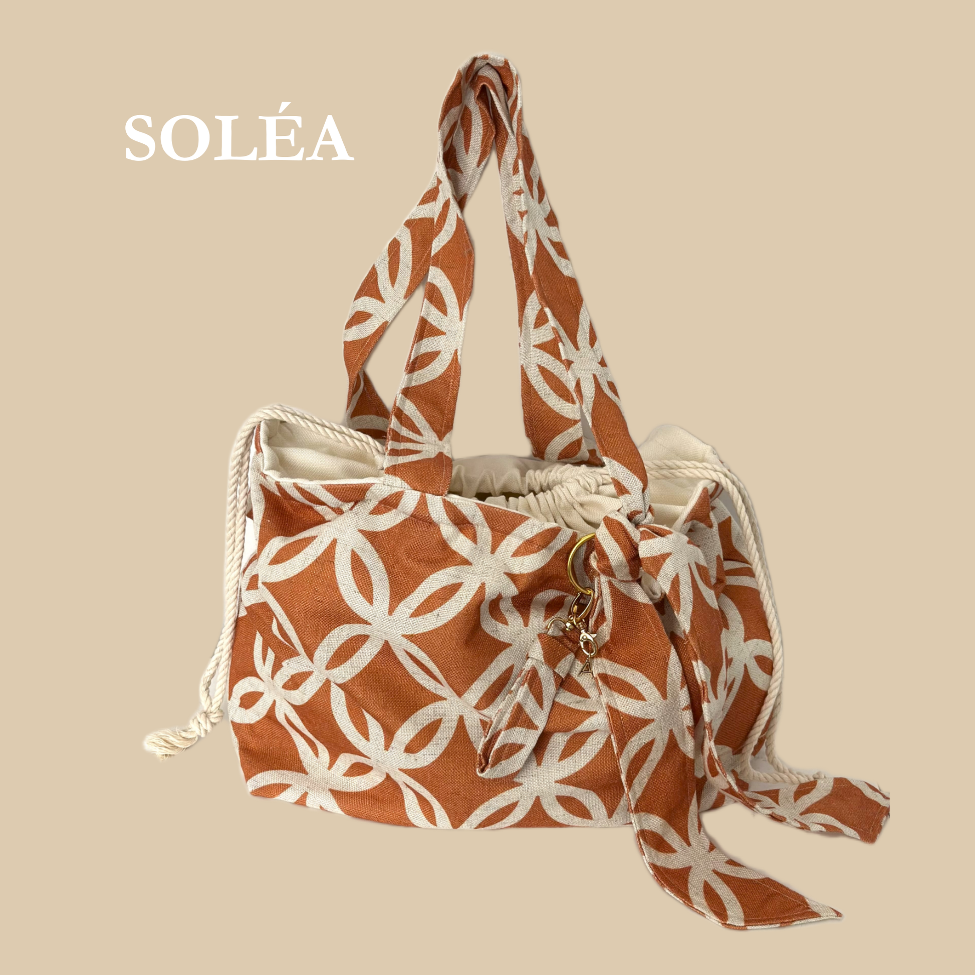 Ensemble Sac de plage SOLÉA fait à la main de façon artisanale au Québec. Le sac est Composé d'un tissu extérieur  en Lin terra cota et crème avec un motif arabesque. L'intérieur du sac est fait d'un coton crème et se referme avec un cordon de serrage de couleur crème. Un foulard pour nouer aux cheveux est suspendu au sac à l'aide d'une anneau dorée pouvant servir d'accessoire bijou au poignet. Inclus un POrte-clés fait du même tissu que le sac fini avec un fermoir à pince doré.